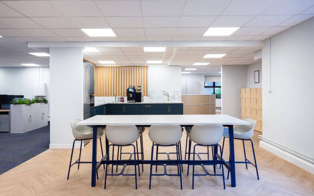 Office Design Trends for 2026 | Fusion Office Design Office kitchen and breakout space in Surrey, using white and navy as the feature colours within poseur height tables and kitchen units, with light oak flooring and woodwork